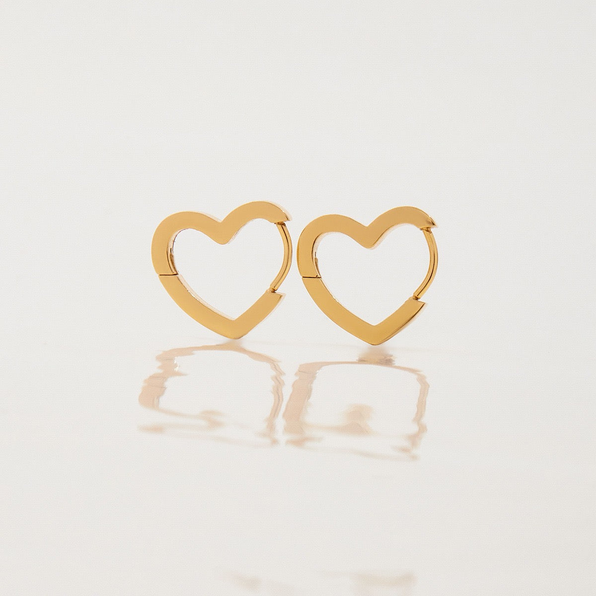 Pair of Love Earrings gold heart huggie earrings on a white background
